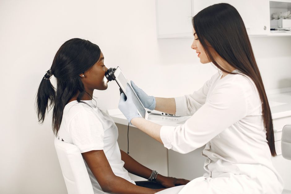 A bright white examination room where a clinician holds an intraoral camera for a seated patient.