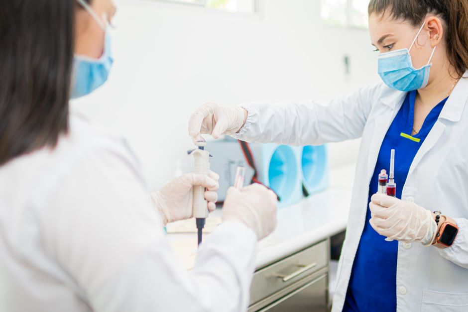 Gloved hands preparing instruments on a clinic worktop, both clinicians masked.