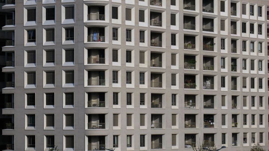 A pale stucco apartment block with recessed balconies and plain railings, photographed from across the street.