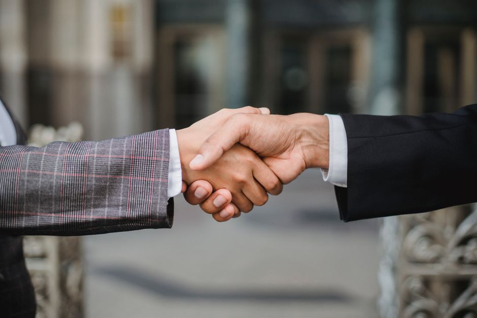 Two people shaking hands outdoors, with a stone building front out of focus behind them.