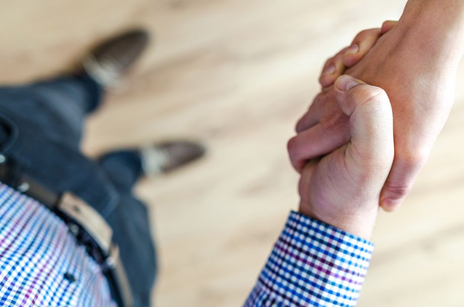 Two people shaking hands, photographed from above over a pale wooden floor.