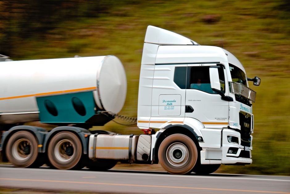 A tanker trailer travelling along a road, panned so the roadside blurs behind it.