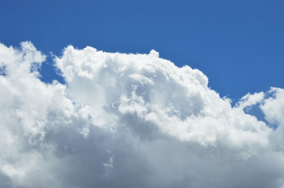 The top of a bank of cumulus cloud, lit from above against deep blue sky.