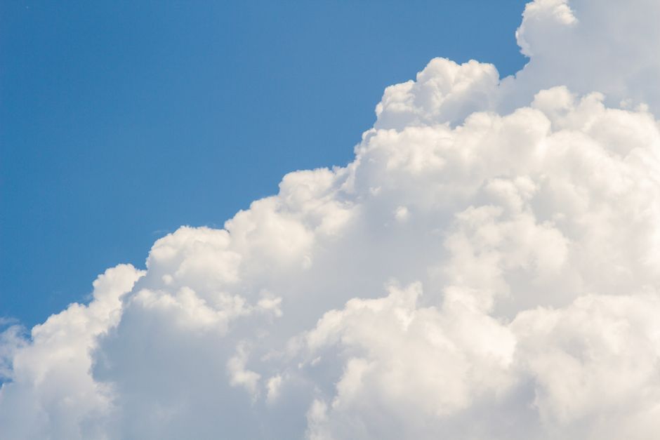 A rising shoulder of white cumulus cloud filling most of a blue sky.